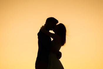 情侣在亲吻日落阿拉巴马州的海滩上
