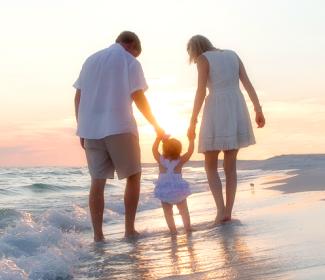 日落时分，年轻的家庭漫步在阿拉巴马州的白色沙滩上