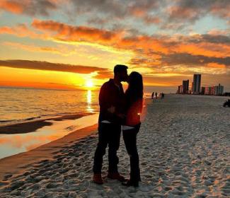 夫妻在日落时分在沙滩上在海湾海岸
