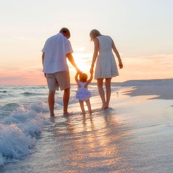 一个年轻的家庭在日落时分沿着阿拉巴马州的白色沙滩散步